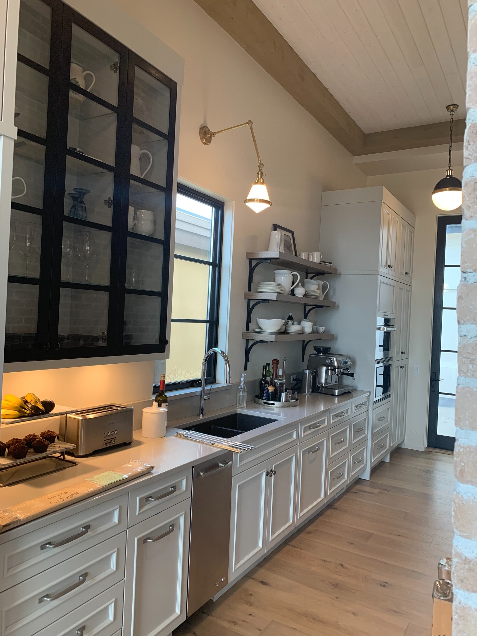 White kitchen cabinet wall with black glass-front cabinets, open shelving, and built-in appliances