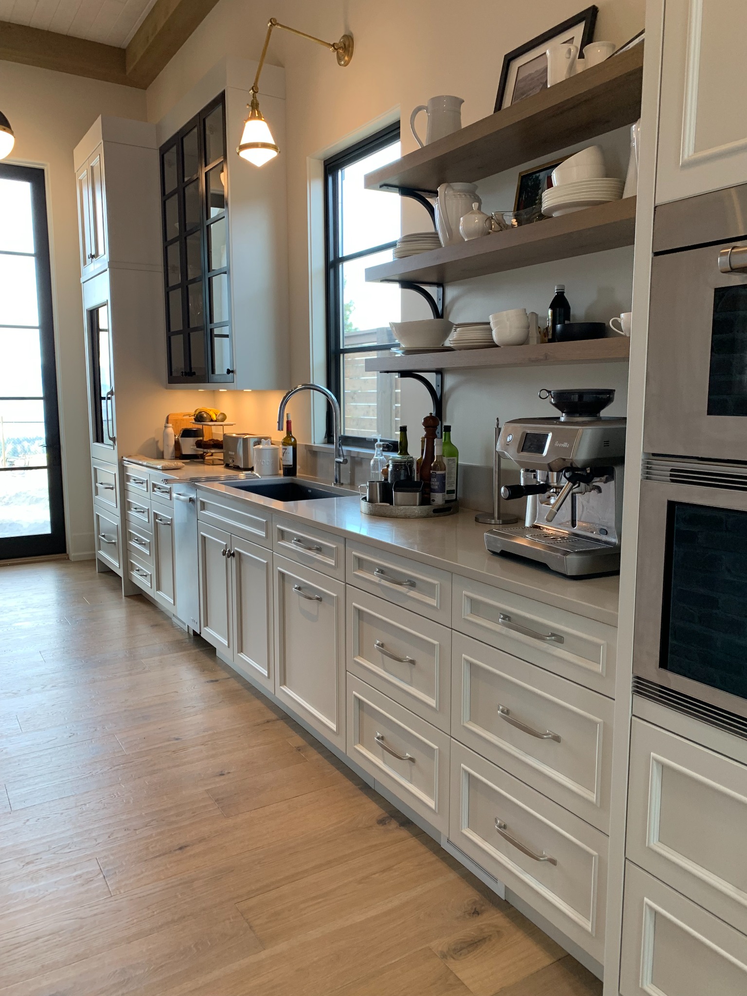 White kitchen cabinetry with open wood shelves, glass-front cabinets, and integrated appliances