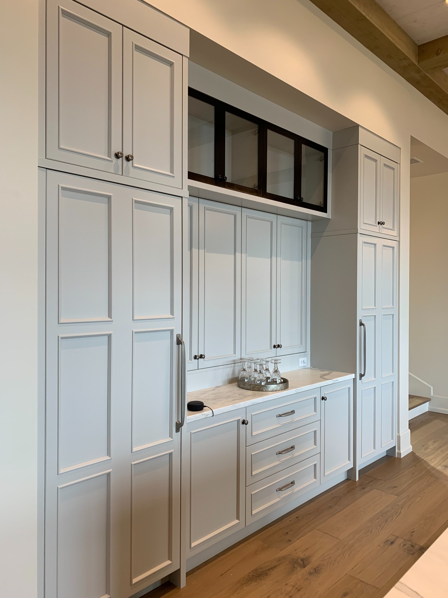 Full-height light gray beverage cabinetry with dark glass-front upper cabinets