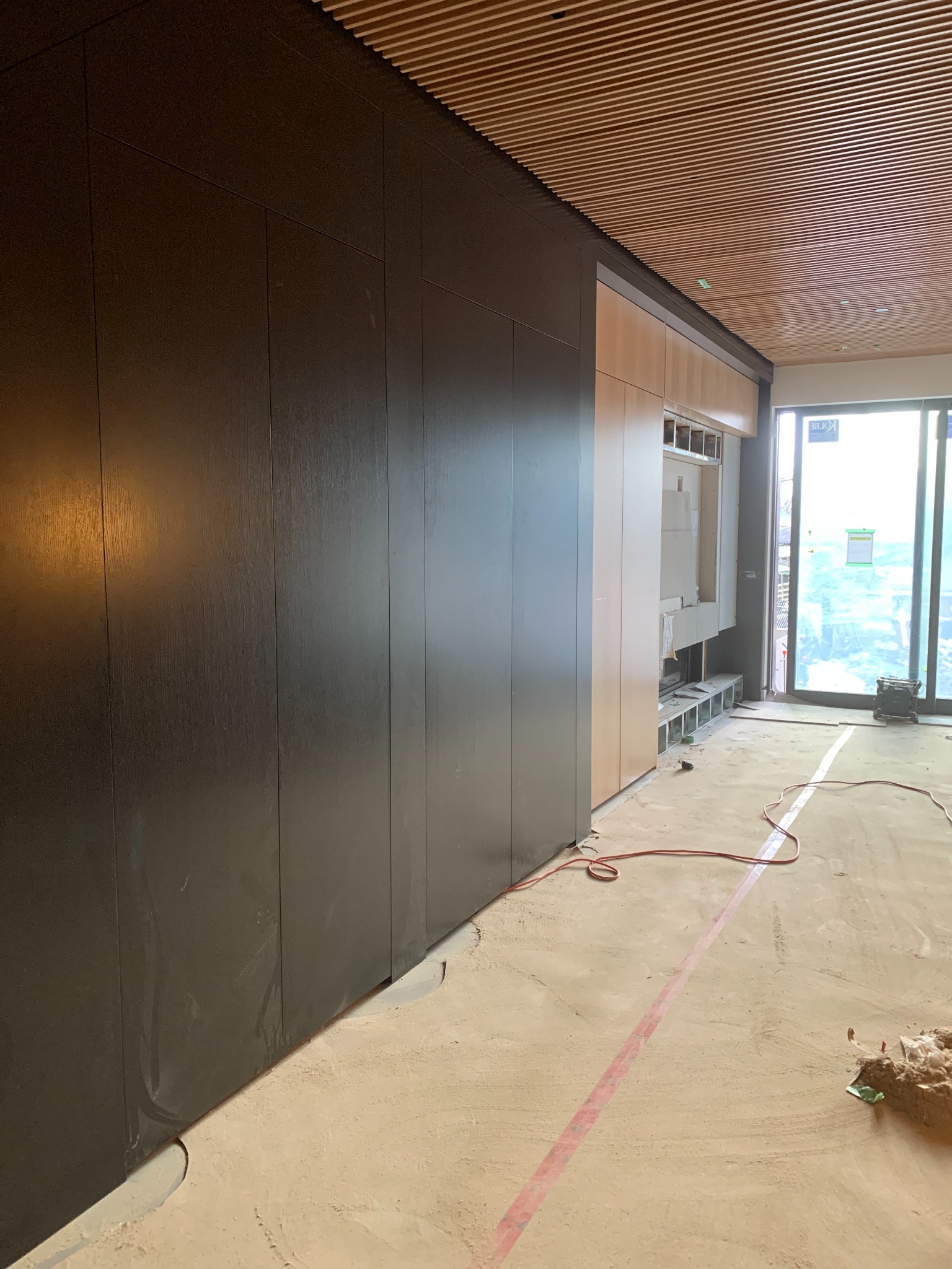 Full-height dark panel wall extending beneath a linear wood ceiling
